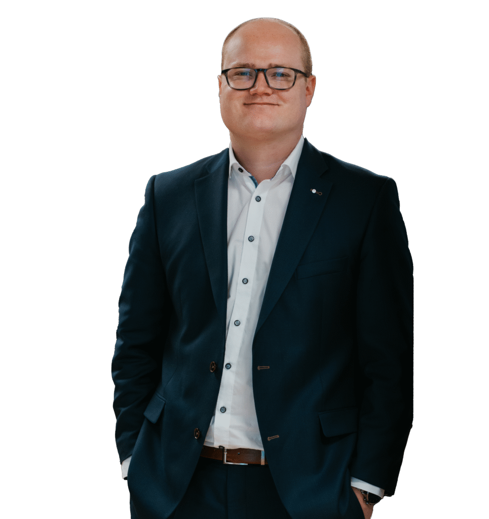 Johannes Schlemmer, Finanzexperte bei tecis, sitzt im Büro an einem Laptop und lächelt in die Kamera.