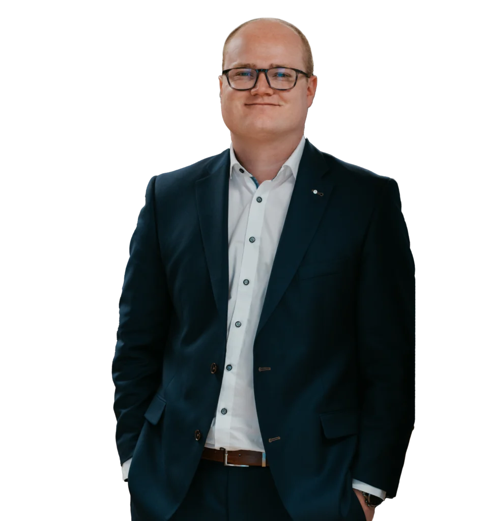 Johannes Schlemmer, Finanzexperte bei tecis, sitzt im Büro an einem Laptop und lächelt in die Kamera.